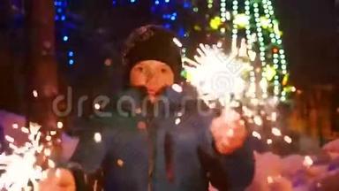 冬天，这个孩子在户外拿着火花。 慢动作。 在圣诞节的背景，灯光和花环